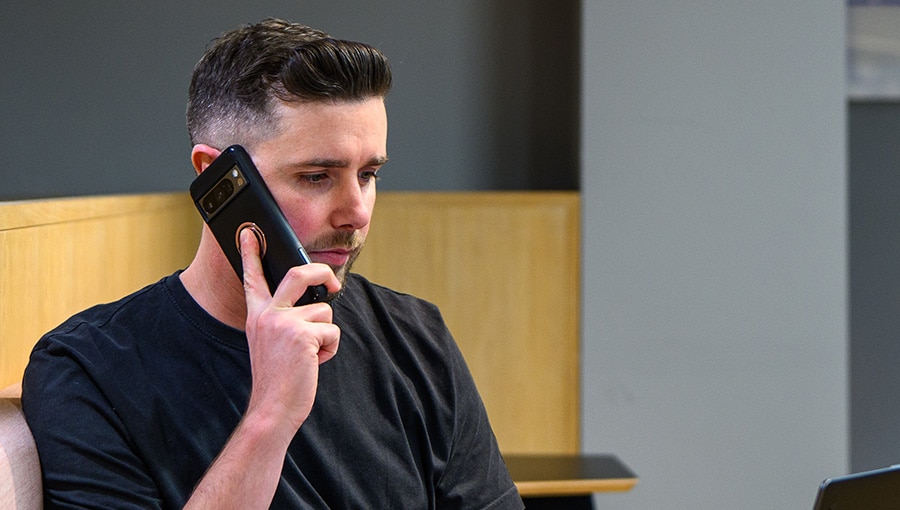 A man sits in an office environment holding a phone to his ear.