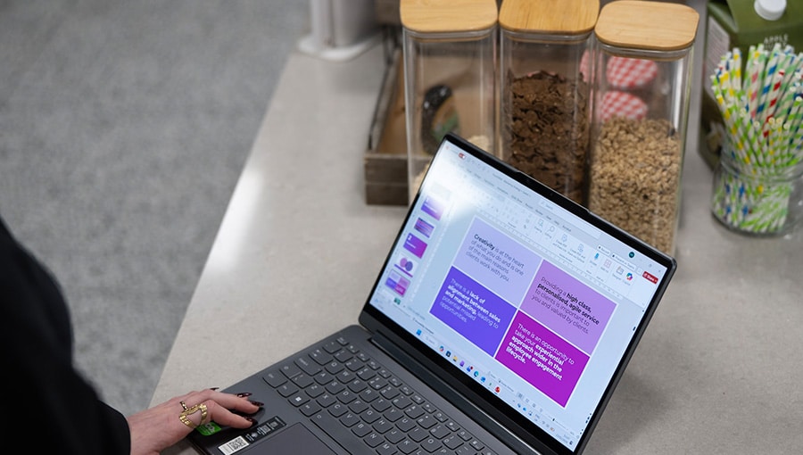 A laptop is shown on somebody's lap. Their hand is just visible. There is a presentation on screen in Kanary Digital's brand colours.