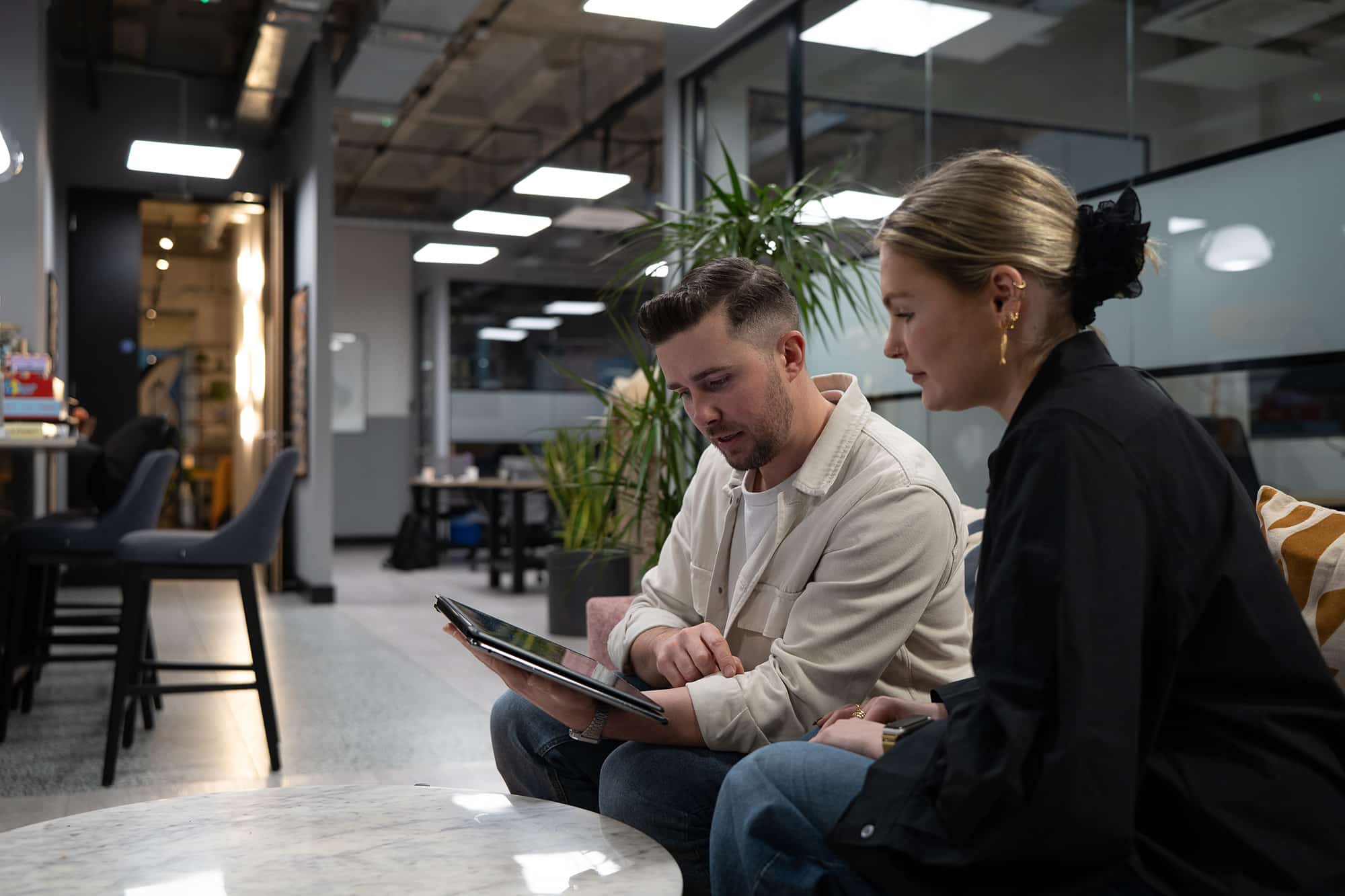 A man and a woman sit in an office environment looking at an iPad during a business meeting